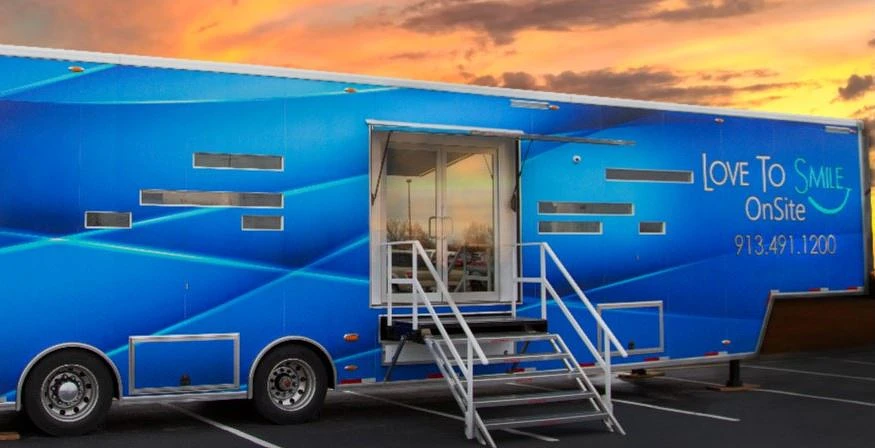 Large blue trailer that houses the mobile dental studio parked in a lot with the sun setting in the background